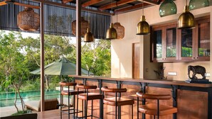 A bar area with wooden stools, a pool view, and hanging brass pendant lights. - Taru Villas Villu - Willpattu (Eluwankulama)