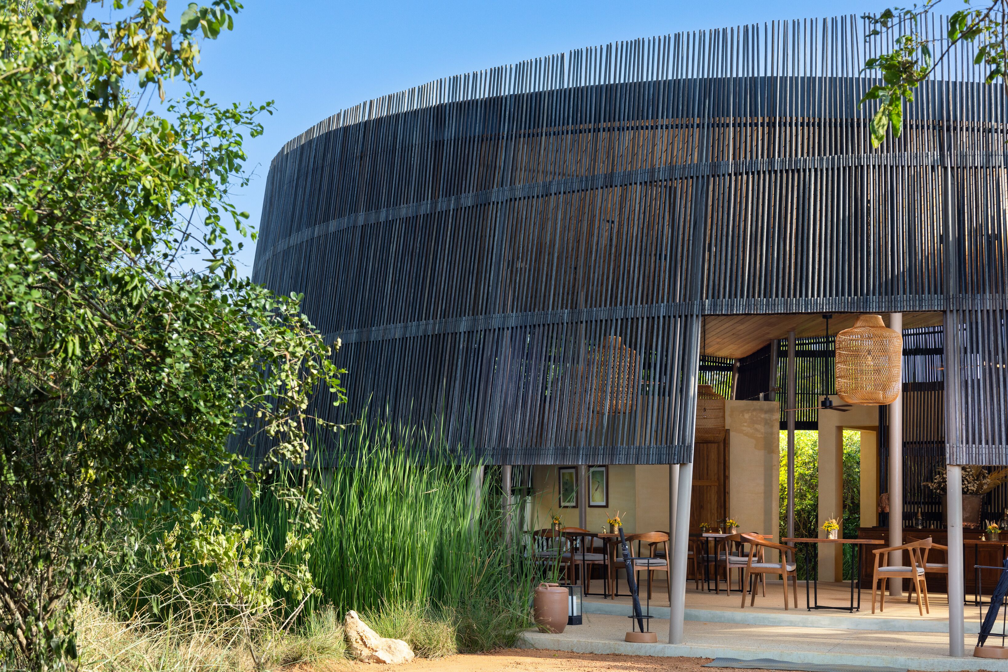 Un bâtiment moderne à la façade incurvée, doté d’un espace extérieur aménagé et de verdure.
