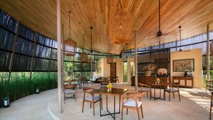 A spacious covered patio with wooden tables and chairs, large hanging wicker lamps, and a view of greenery outside. - Taru Villas Villu - Willpattu (Eluwankulama)