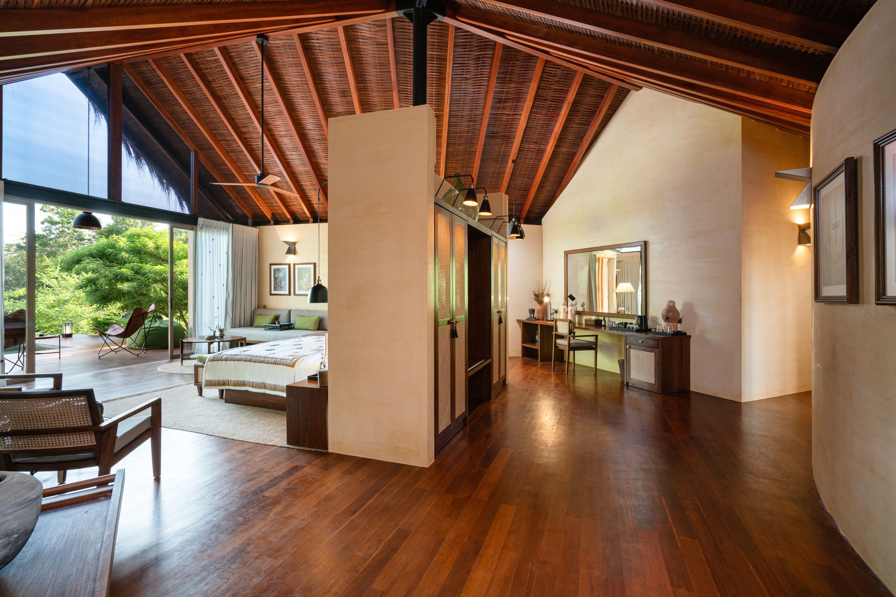 A spacious room with a wooden ceiling, large windows, a bed, a desk, and a mirror.