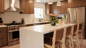 Une cuisine moderne avec des meubles en bois, un réfrigérateur en acier inoxydable, un grand îlot central doté de tabourets et un vase rempli de fleurs.