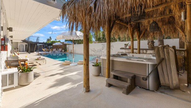 Un espace piscine doté d’un jacuzzi, de chaises longues et d’une structure recouverte d’un toit de chaume.