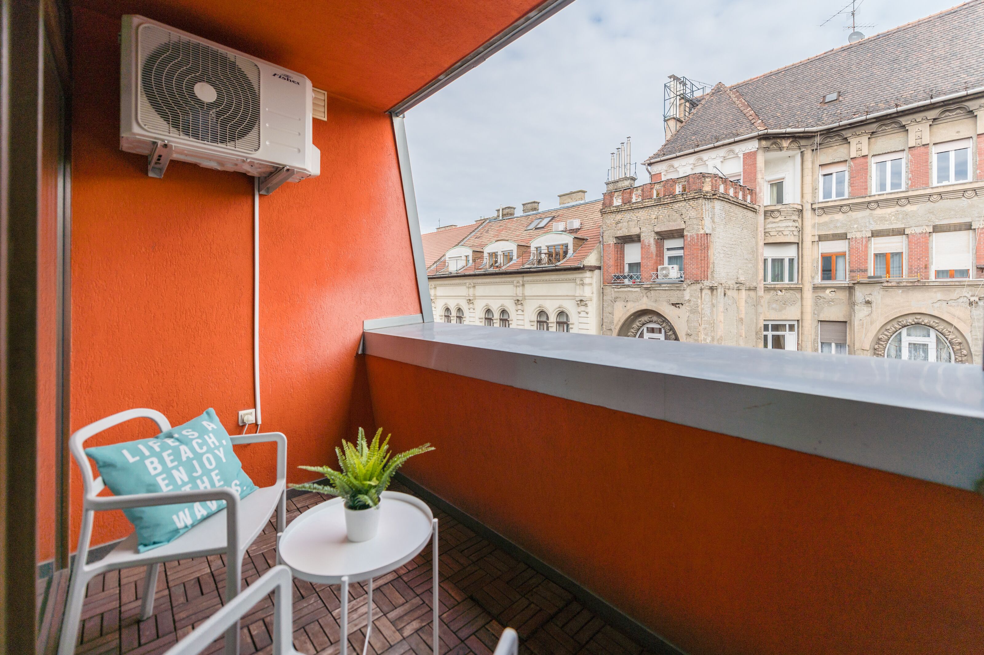 A balcony with a white chair, a small table with a plant, and an air conditioning unit.