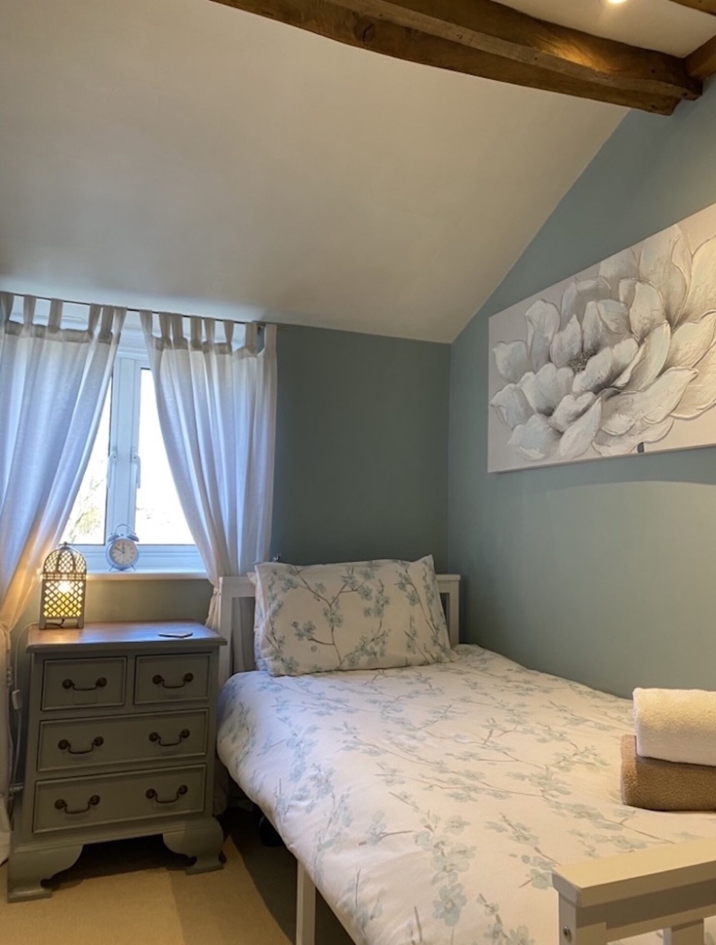 Un dormitorio con una cama, una mesita de noche, una lámpara y un cuadro colgado en la pared.