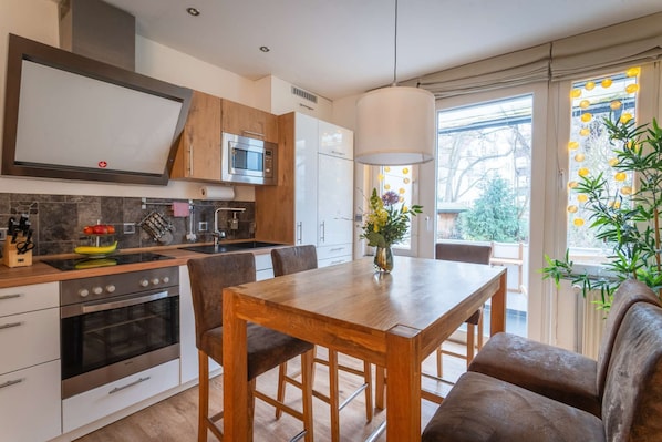 A modern kitchen with a dining area, stainless steel appliances, and a view of the outdoors.