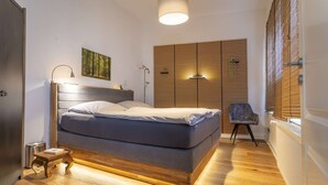 Un dormitorio moderno con una cama grande, una mesita de noche, una lámpara, una silla y un panel de pared de listones de madera.