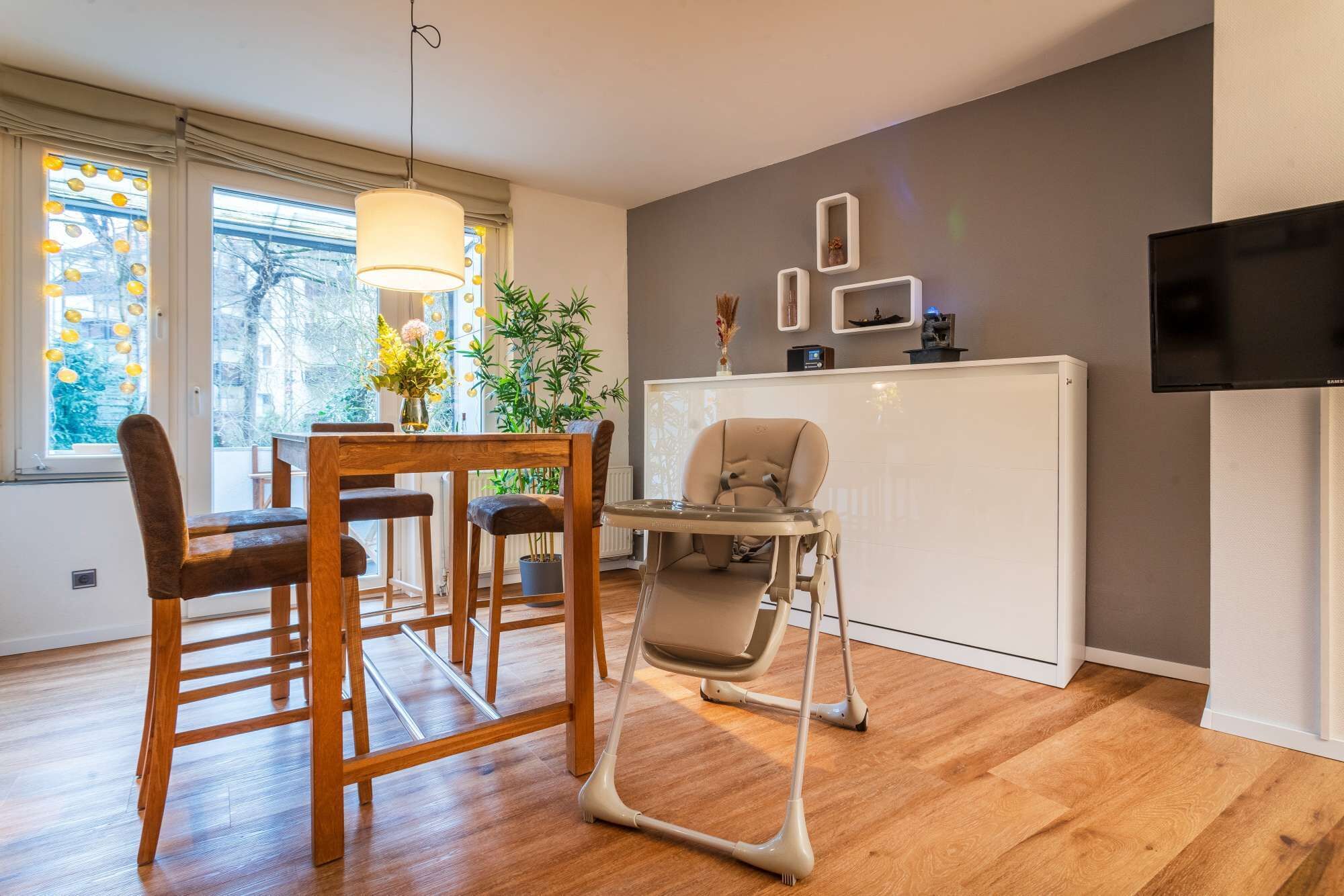 Ein modernes Wohnzimmer mit Essbereich, Hochstuhl und Fernseher an der Wand.