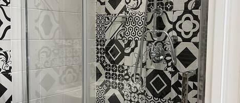 A shower with a glass door, a sink, and patterned tiles.