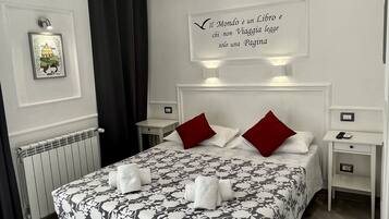 Une chambre d’hôtel moderne avec un grand lit, deux oreillers rouges, une tête de lit blanche et une citation encadrée accrochée au mur.