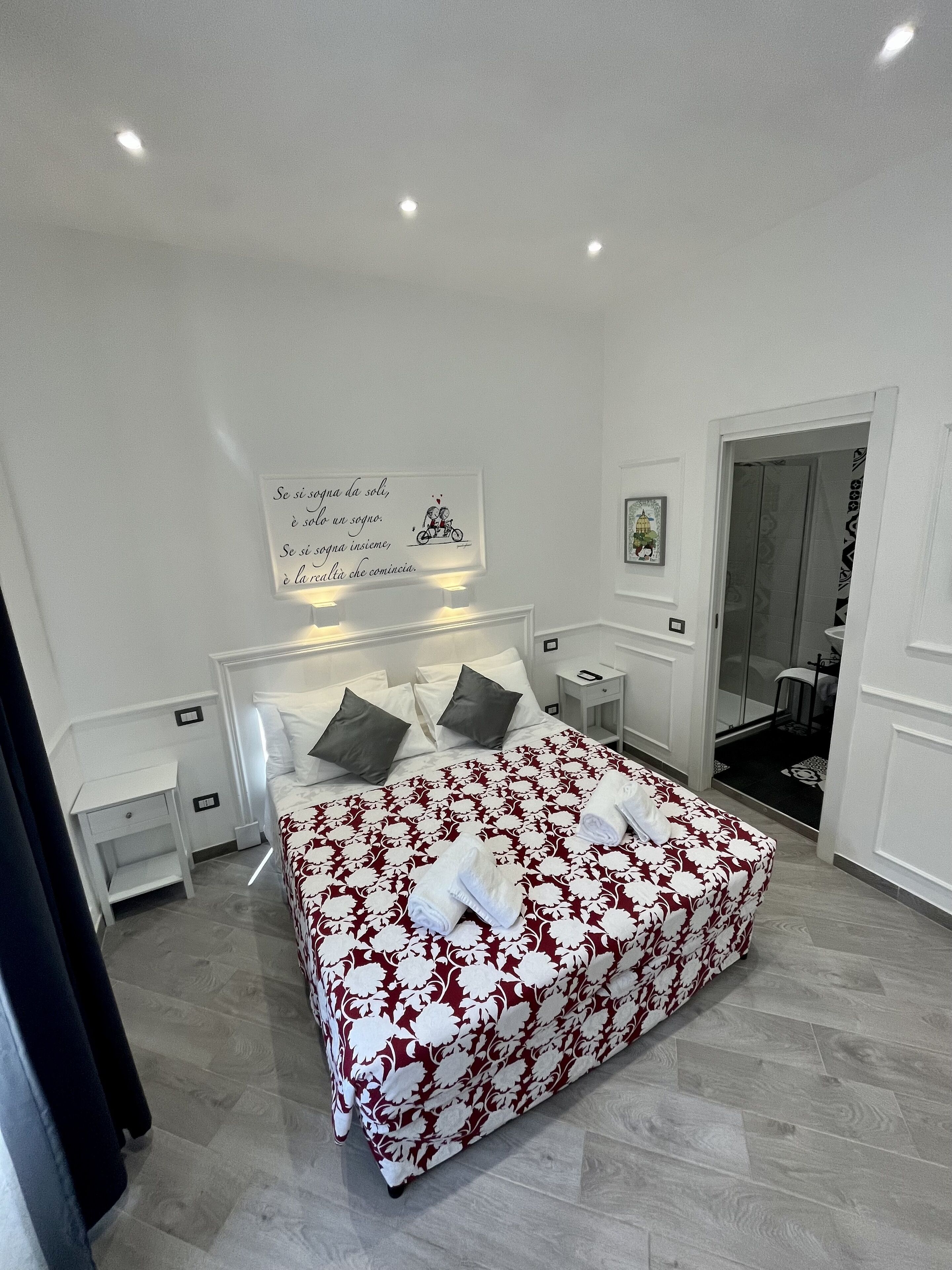 A neatly arranged bedroom with a large bed, a bedside table, a nightstand, and a wall-mounted sign.