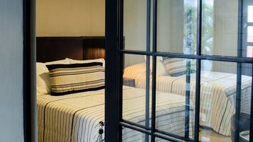 A hotel room with a large sliding glass door leading to a balcony. The room has two beds with striped bedding and a dark headboard.