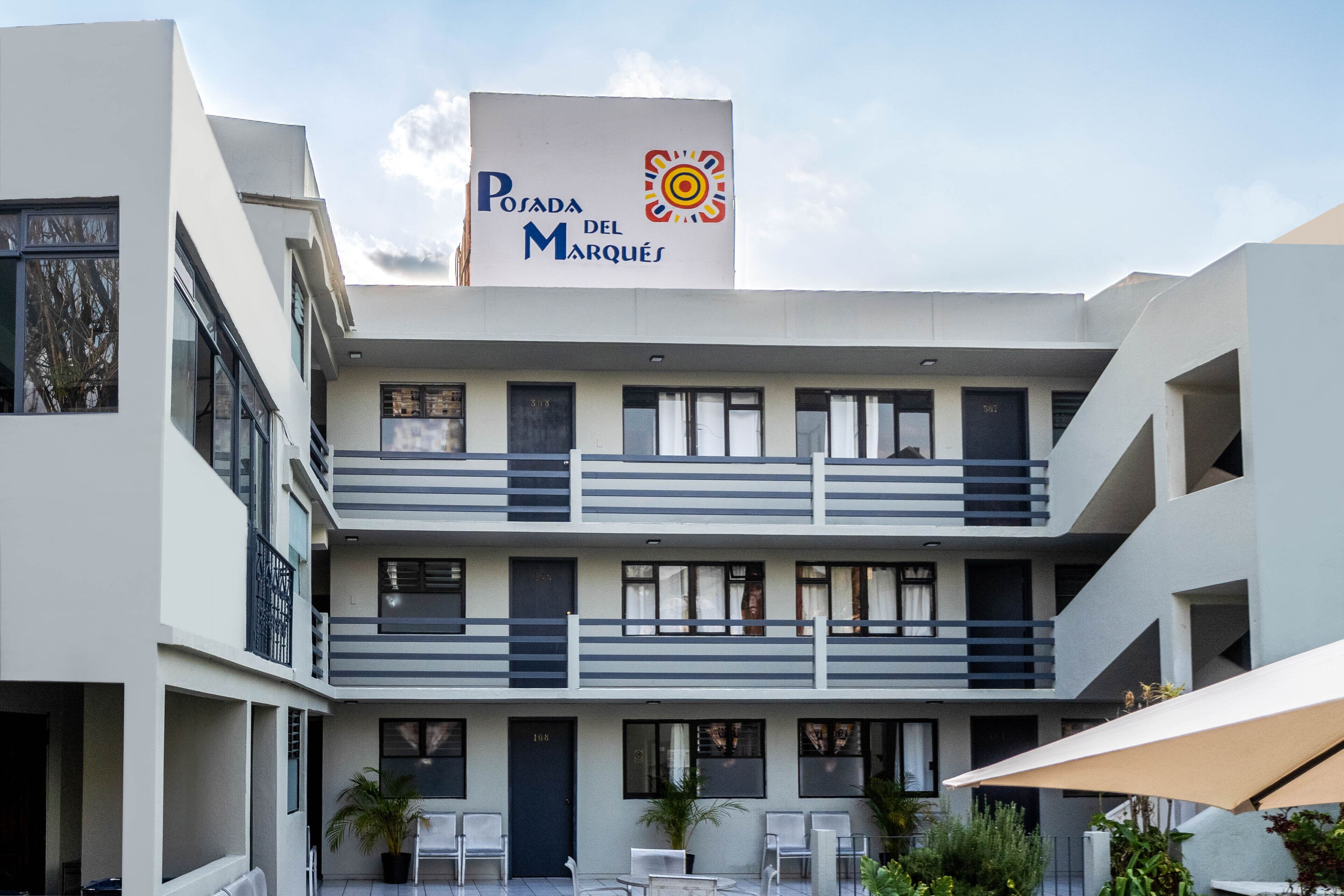 Un hotel moderno con un cartello che riporta "Posada del Marqués". Si nota una struttura a più piani con balconi e un cortile con posti a sedere all'aperto.