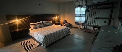 A modern bedroom with a large bed, a desk, a chair, a ceiling fan, and a window with curtains.