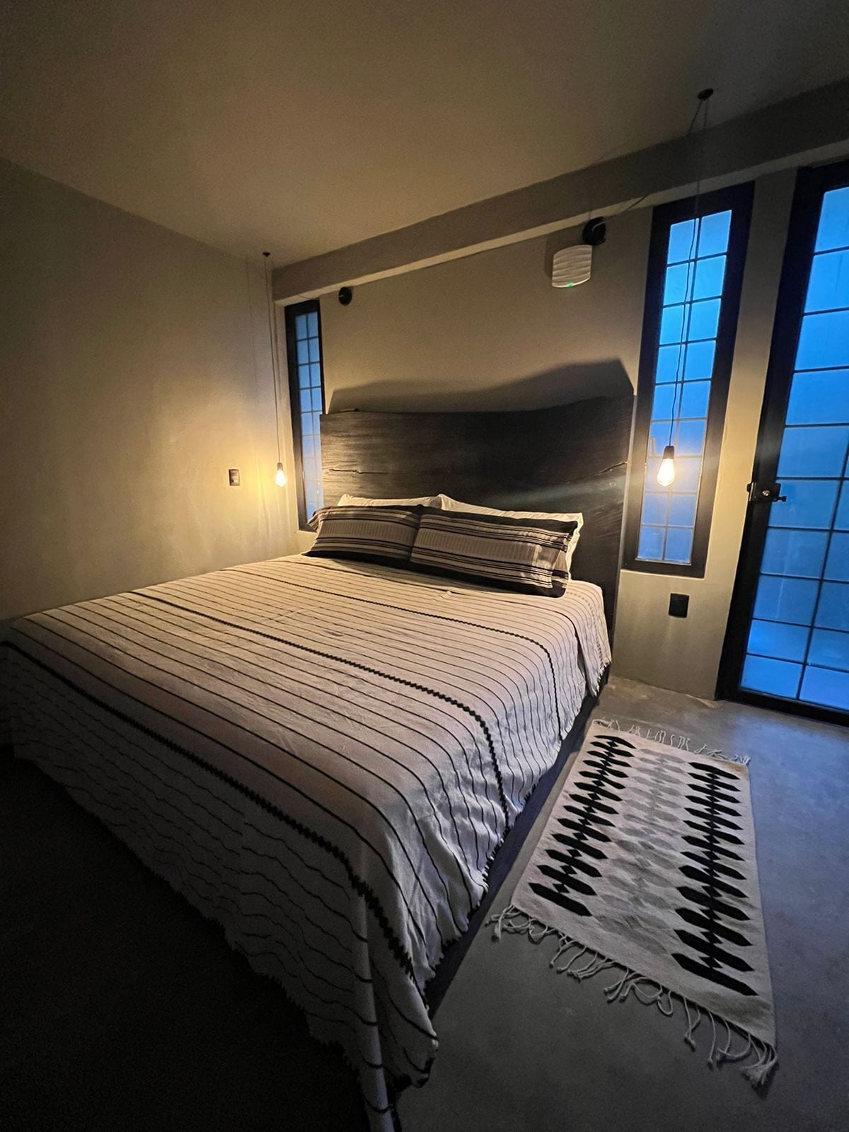 A bedroom with a large bed, two bedside lamps, a window with blinds, and a rug.