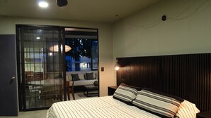 A bedroom with a bed, a nightstand, a lamp, a sliding glass door leading to a balcony, and a view of the outside. - Lofts Marques Oaxaca (Oaxaca)