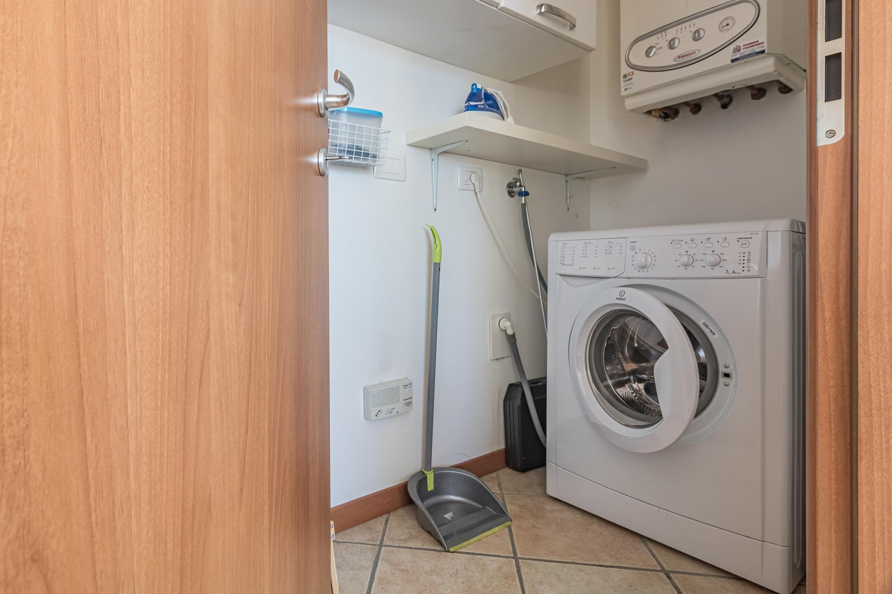 Una sala de lavandería con una lavadora, un trapeador y un estante sobre la lavadora.