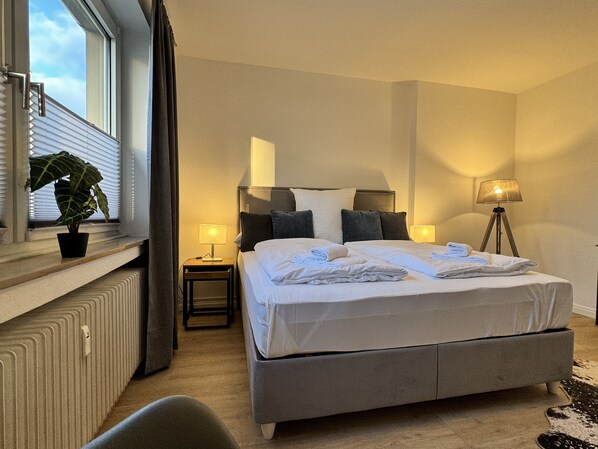 A hotel room with a bed, bedside lamps, a potted plant, and a radiator. - Wagner CITY-Apartment mit Netflix (Bielefeld)