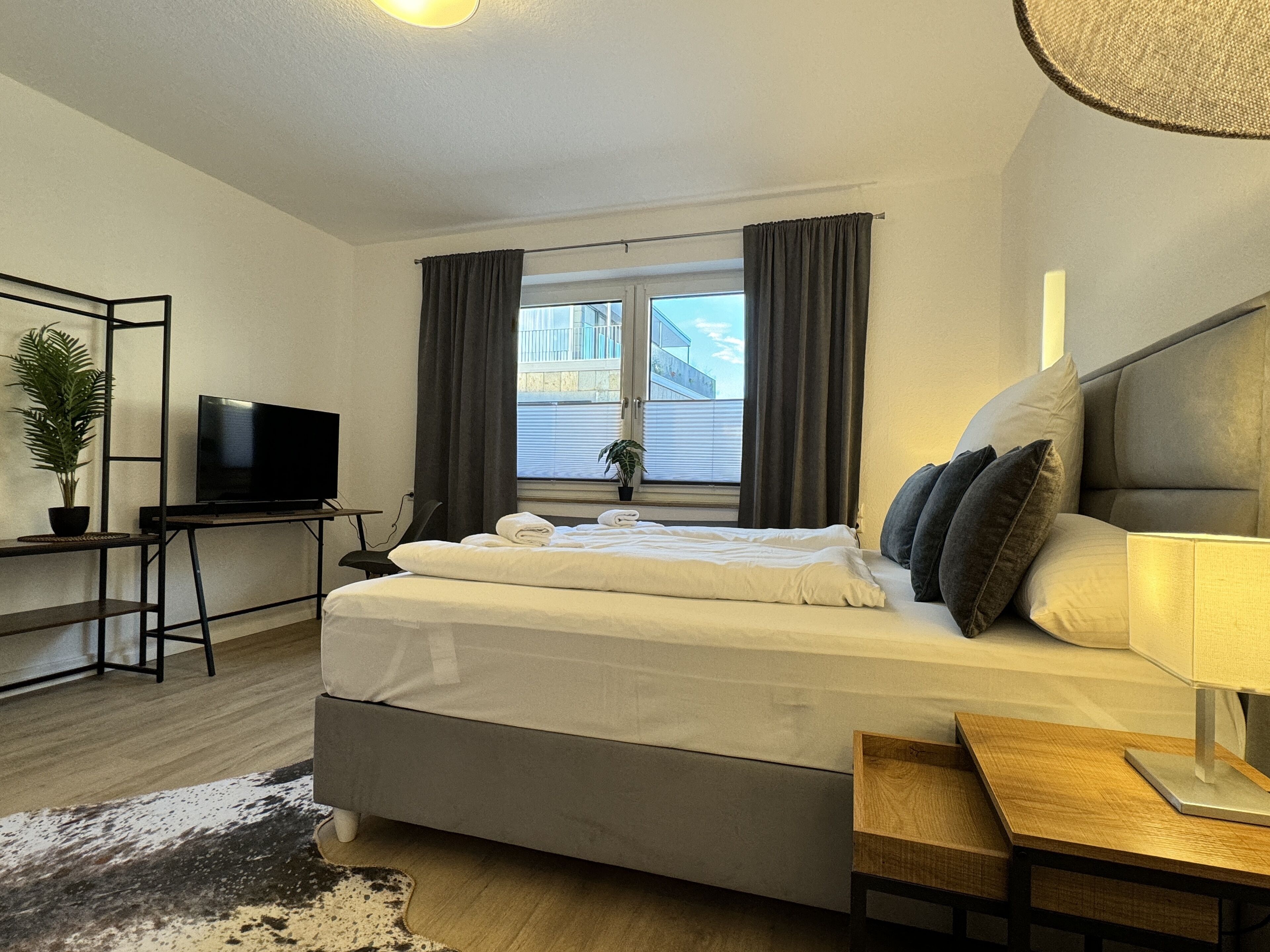 Una habitación de hotel moderna con una cama grande, televisión, escritorio y ventana con cortinas.