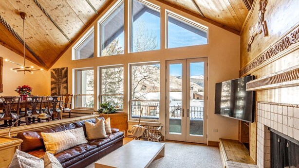 A spacious living room with a high ceiling, large windows, a fireplace, and a television.