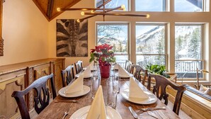 A dining area with a long wooden table set for a meal, large windows with a mountain view, and a modern light fixture above the table.