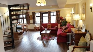 A spacious living room with a staircase, a red sofa, a wooden coffee table, and a bookshelf.