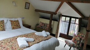 A bedroom with a large bed, floral-patterned bedding, a wooden ceiling, and a window with curtains.