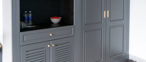 A grey wardrobe with multiple shelves and a lower cabinet, a bowl on the top shelf, and a pair of shoes on the floor.