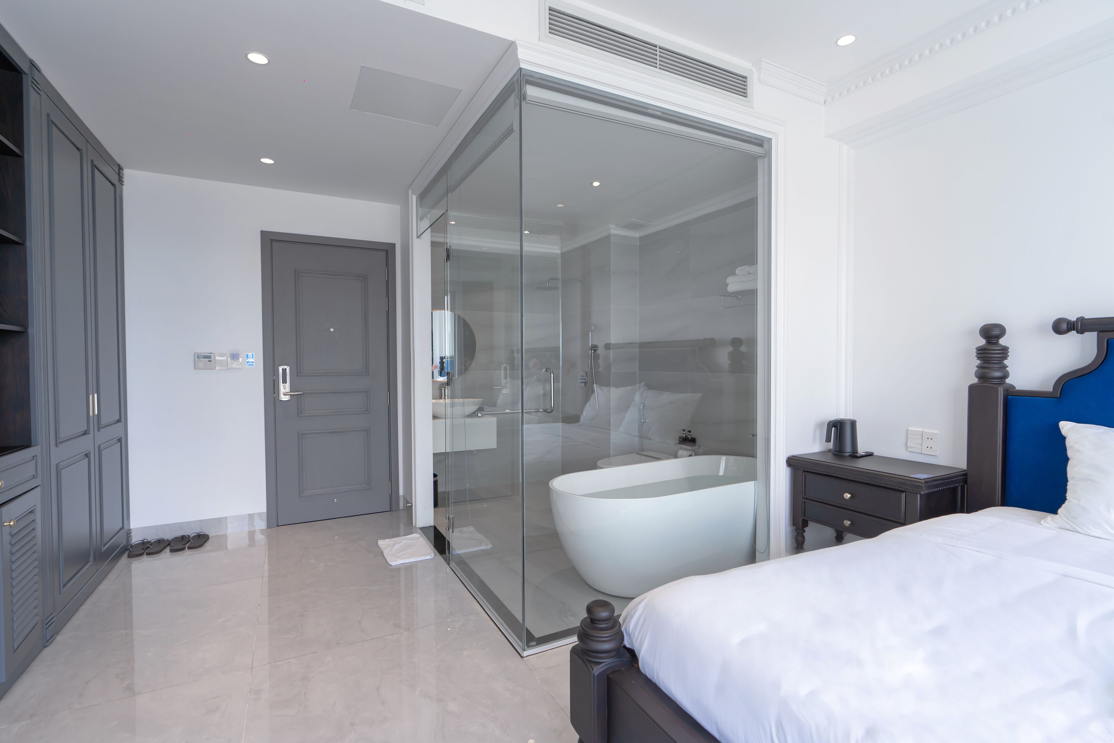 Een moderne hotelkamer met een groot bed, een douchecabine met glazen wanden, een nachtkastje met lamp en een kledingkast.