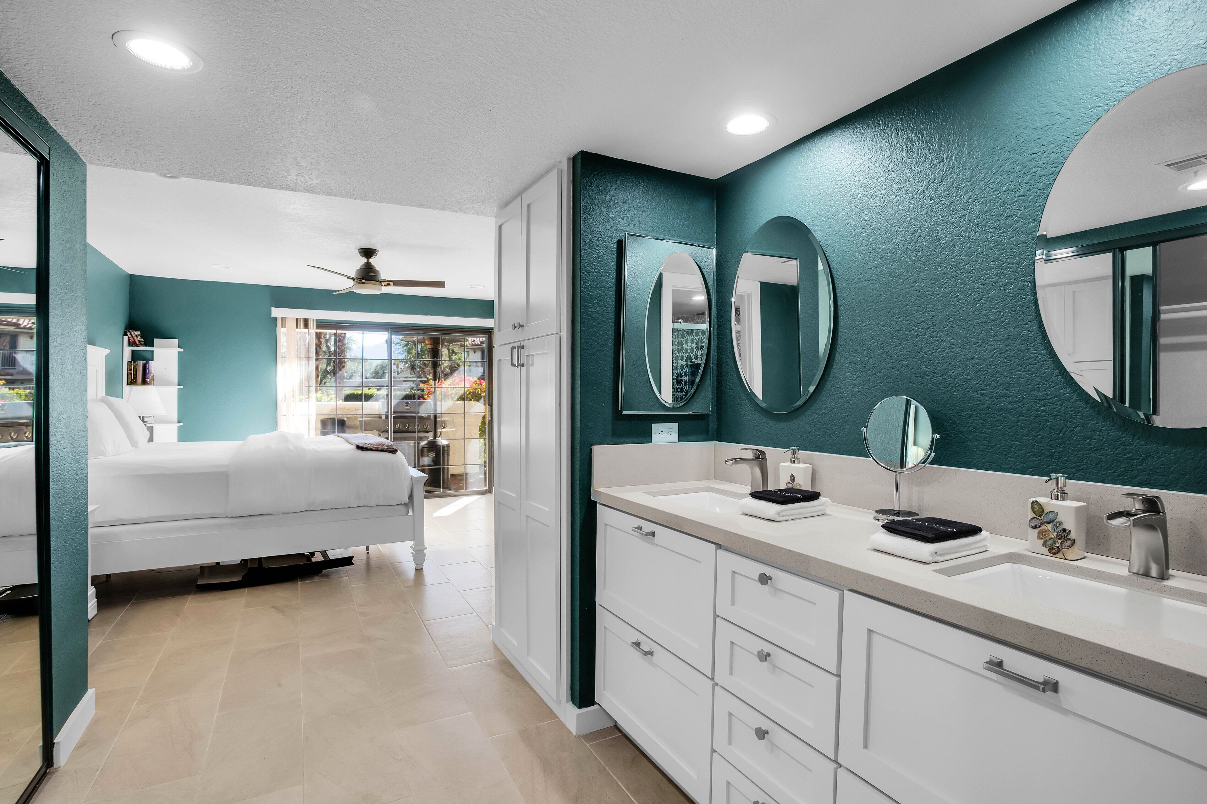 A modern bedroom with a bed, a white dresser, and a bathroom with a sink and mirrors.