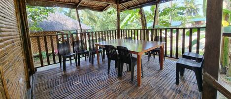 A covered outdoor area with a wooden table and chairs, surrounded by a wooden railing.