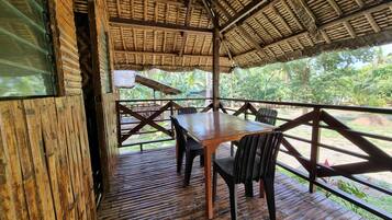An outdoor wooden deck with a thatched roof, a wooden table, and wicker chairs.