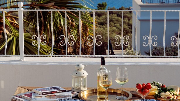 A table set with plates, glasses, and a bottle, overlooking a coastal view with a sailboat and buildings. - Villa Olivia is on the corner of one of the prettiest streets in Kalkan (kas)