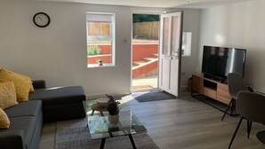 Ein modernes Wohnzimmer mit einer Couch, einem Couchtisch, einem Fernseher und einer Schiebetür zu einem Außenbereich.