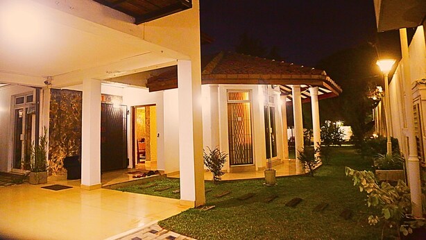 A modern house with a covered patio, a well-maintained lawn, and a gated entrance. - Ared Villa (Seeduwa - Katunayake)