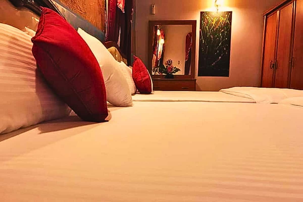 A hotel room with a bed, pillows, a nightstand, a mirror, and a painting on the wall.