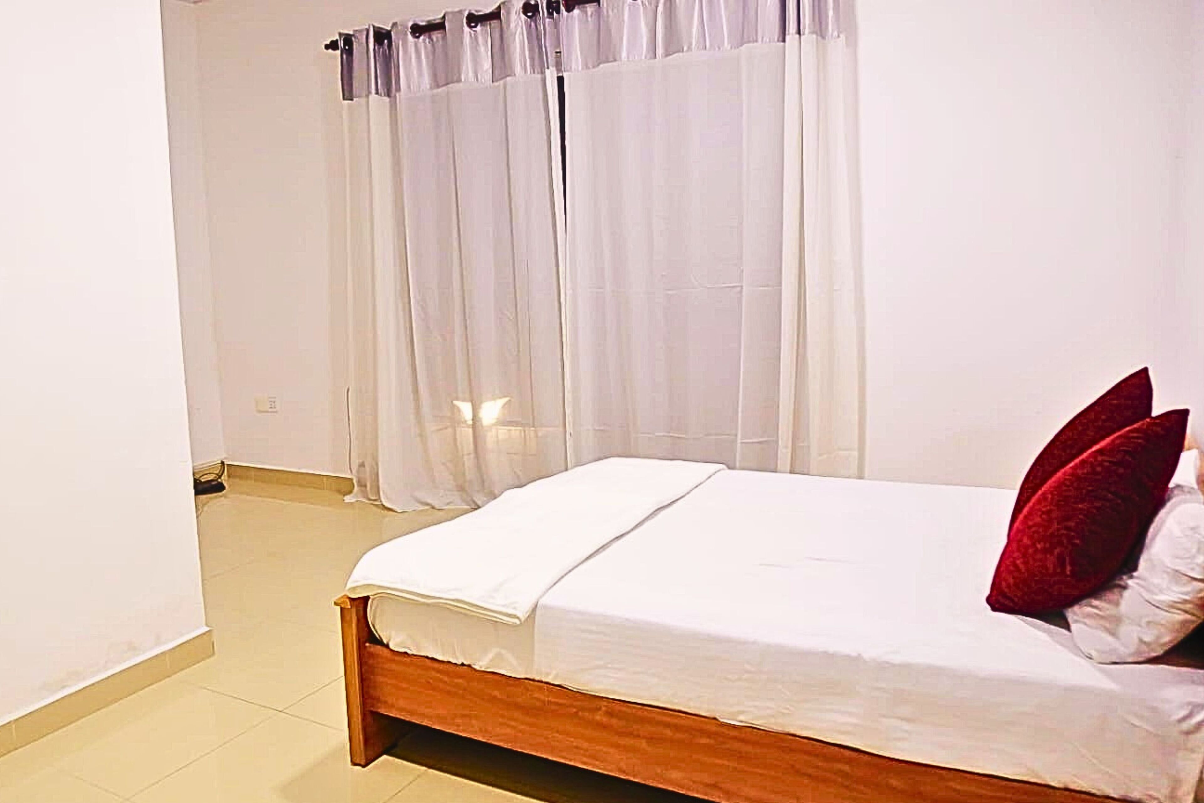 Un dormitorio con cama de madera, ropa de cama blanca y almohadas rojas.