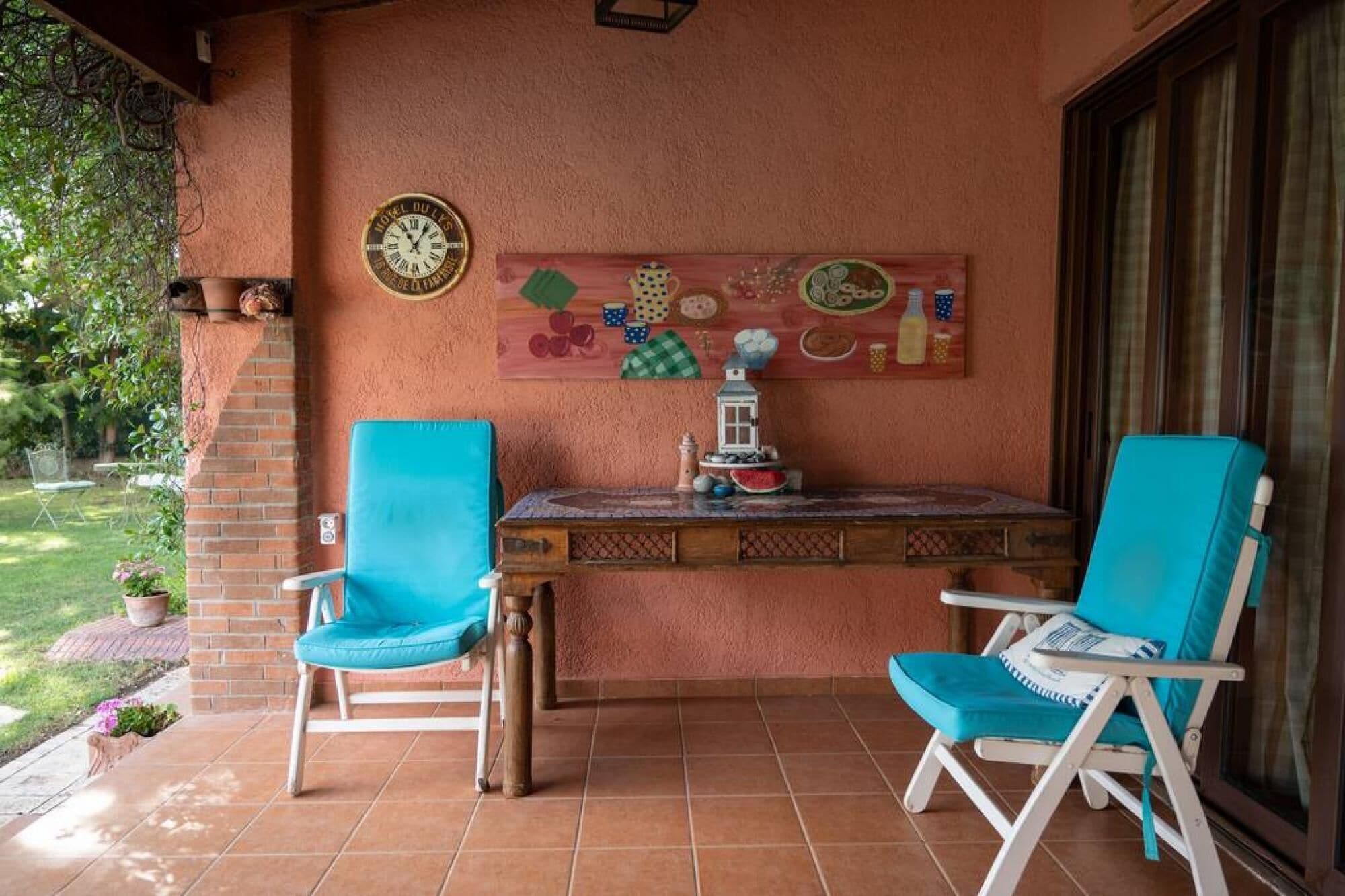 Un patio con dos sillas turquesas, una mesita y un reloj de pared.