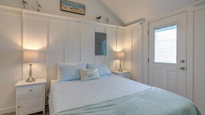 Un dormitorio con cama, mesitas de noche, lámparas, una puerta y adornos de pájaros en la pared.