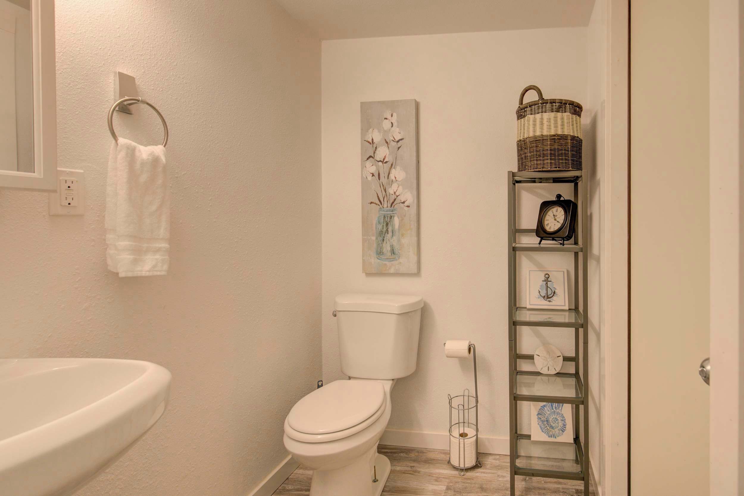 A bathroom with a toilet, sink, towel rack, and a shelf with a basket and clock.
