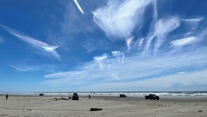 Una playa con cielo despejado, algunas personas y vehículos en la arena.