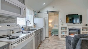 Cocina compacta con microondas, estufa y refrigerador, que da paso a un dormitorio con televisor y chimenea.