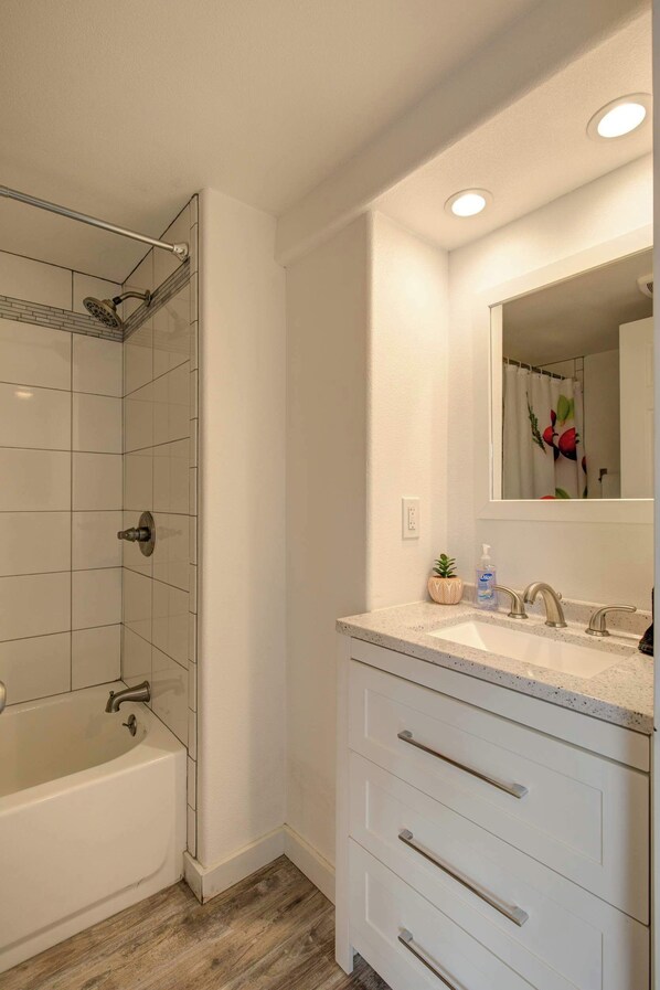 Un baño moderno con bañera, ducha, lavabo con espejo y una pequeña planta en maceta.