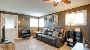 A living room with a leather sofa, a wooden coffee table, a black leather chair, a TV, and a ceiling fan. - Affordable Grayland Beach Stay – Ocean Spray 6 (Grayland)