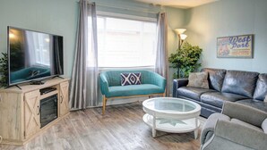Un salon avec une télévision, un canapé, une table basse et un panneau accroché au mur.