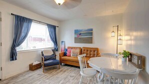 A room with a window, a sofa, a dining table, and a lamp.