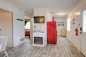 A room with a fireplace, a red refrigerator, a television, and a wooden cabinet.