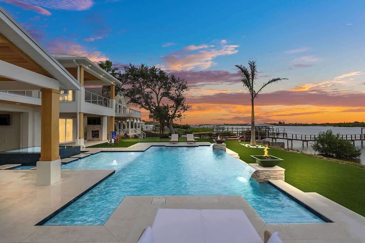 Modern waterfront pool area with fire features and sunset views.