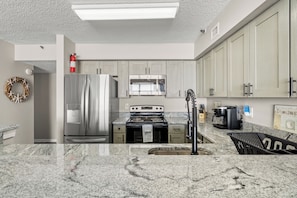 Una cocina moderna con encimeras de granito, electrodomésticos de acero inoxidable y armarios de madera clara.