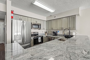 A modern kitchen with stainless steel appliances, granite countertops, and light wood cabinets.