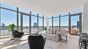 A spacious living room with large windows, a black chair, a sofa, and a dining area. - West Loop PH: Unmatched Views & Private Deck (Chicago)